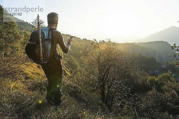 Älterer Mann benutzt sein Smartphone  während er bei Sonnenaufgang auf einem Berg steht  Orobie  Lecco  Italien