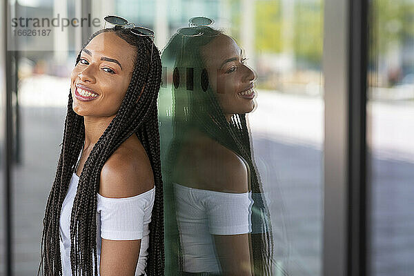 Junge Frau lehnt lächelnd an einer Glaswand in der Stadt