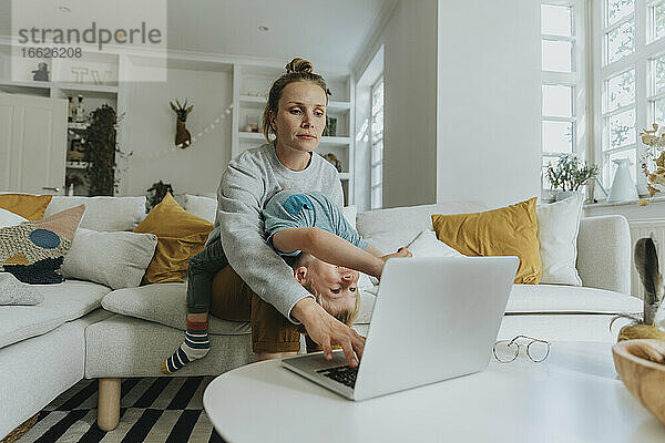 Die Mutter kümmert sich um den Jungen  während sie zu Hause am Laptop arbeitet