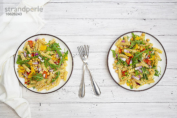 Zwei Teller mit vegetarischem Nudelsalat mit Kichererbsen  Paprika  Rucola  Zwiebel  Petersilie und Basilikum