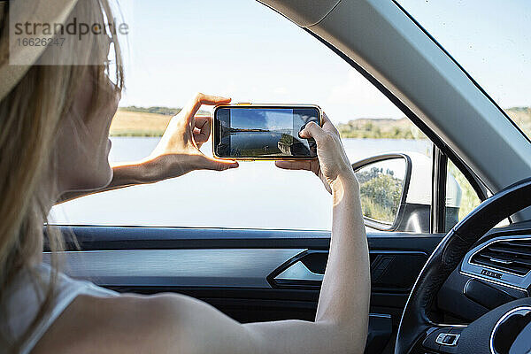 Junge Frau  die im Auto sitzend mit dem Handy fotografiert