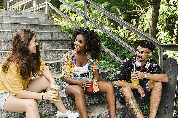 Freunde sitzen auf den Stufen und trinken Saft in einem öffentlichen Park