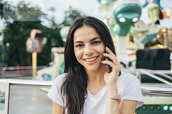 Nahaufnahme einer lächelnden Frau  die in einem Vergnügungspark über ein Smartphone spricht