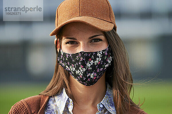 Junge Frau mit Mütze und Gesichtsmaske steht in der Stadt