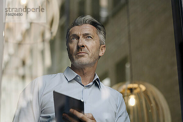Mann  der ein digitales Tablet benutzt  während er an einer Glaswand im Büro steht