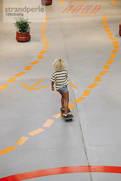 Blonde Frau fährt Skateboard auf einem Fußweg mit orangefarbener Straßenmarkierung