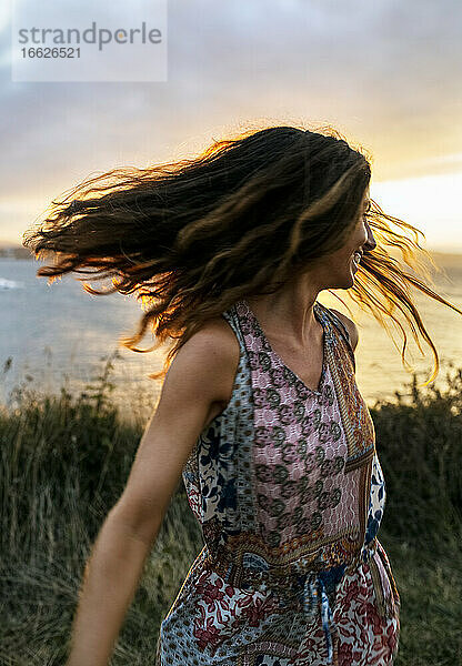 Fröhliche junge Frau  die bei Sonnenuntergang ihr Haar gegen den Himmel wirft