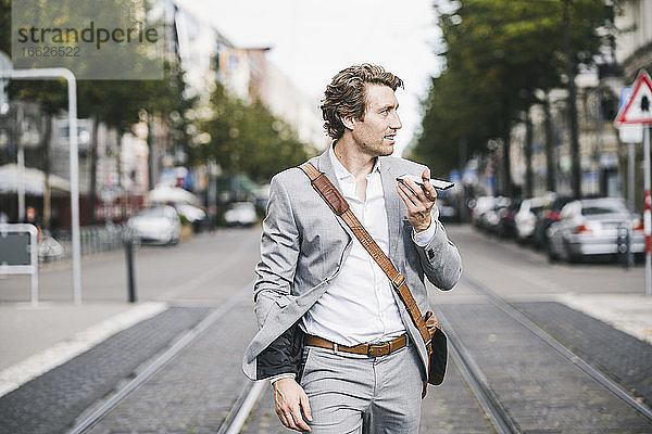 Lächelnder Geschäftsmann  der mit seinem Handy telefoniert  während er in einer Straßenbahn in der Stadt spazieren geht