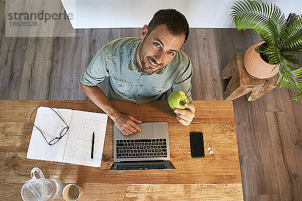 Lächelnder Geschäftsmann mit frischem Apfel bei der Arbeit zu Hause