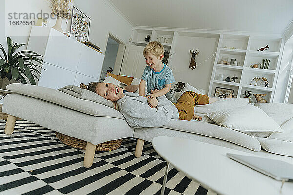 Lächelnde Mutter und Junge spielen auf dem Sofa zu Hause