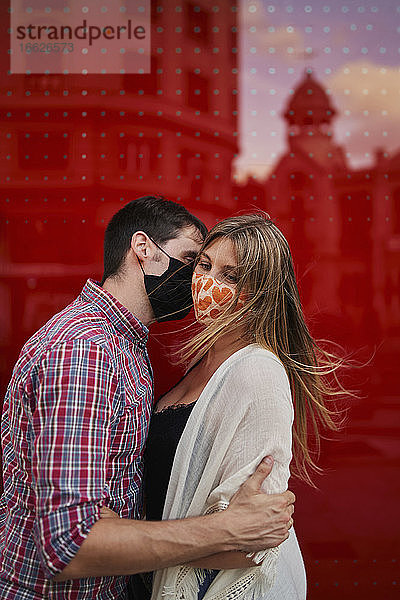 Paar küsst sich mit Schutzmaske vor roter Acrylwand