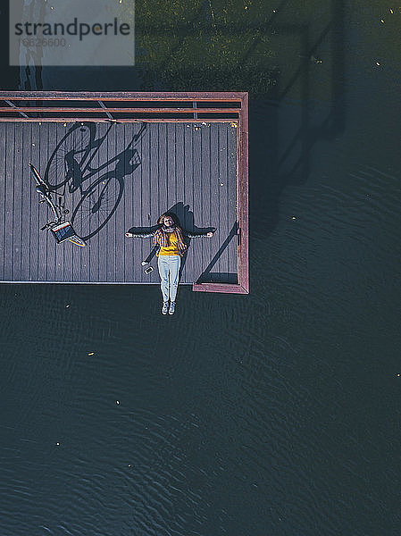 Luftaufnahme einer jungen Frau  die auf dem Rücken liegend am Rande eines Stegs an der Küste steht
