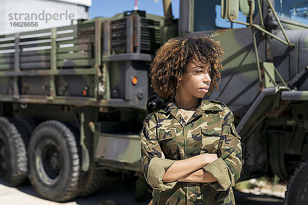 Junge Soldatin mit verschränkten Armen  die wegschaut  während sie an einem Lastwagen auf einem Militärstützpunkt steht