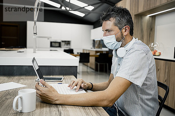 Geschäftsmann mit Schutzmaske bei der Arbeit am Laptop im Büro während der COVID-19-Pandemie