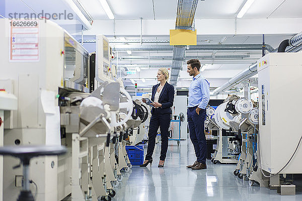 Männlicher Techniker steht neben einer Geschäftsfrau  die in einer Fabrik Maschinen analysiert