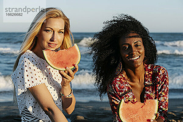 Freunde essen ein Stück Wassermelone am Strand an einem sonnigen Tag
