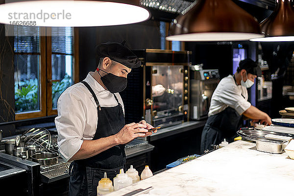 Chefkoch schreibt Textnachrichten auf seinem Smartphone  während er in der Restaurantküche steht