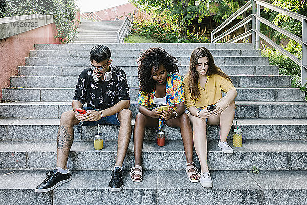 Junge Freunde schreiben SMS auf dem Smartphone  während sie auf den Stufen im Park sitzen