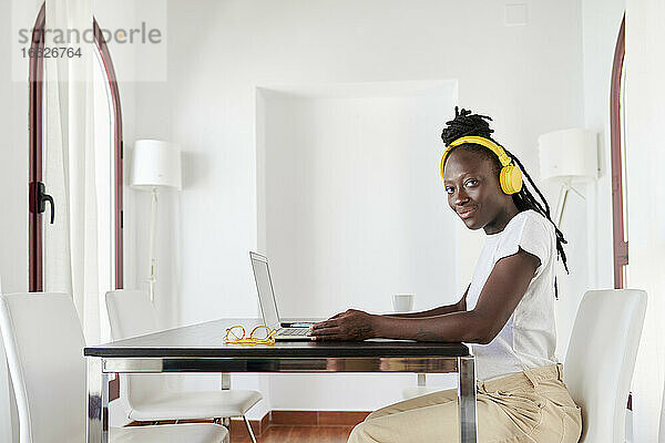 Junge Frau mit Kopfhörern und Laptop auf dem Schreibtisch im Heimbüro
