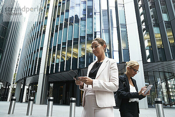 Reife Geschäftsfrauen mit Smartphones gegen moderne Büro-Wolkenkratzer im Stadtzentrum