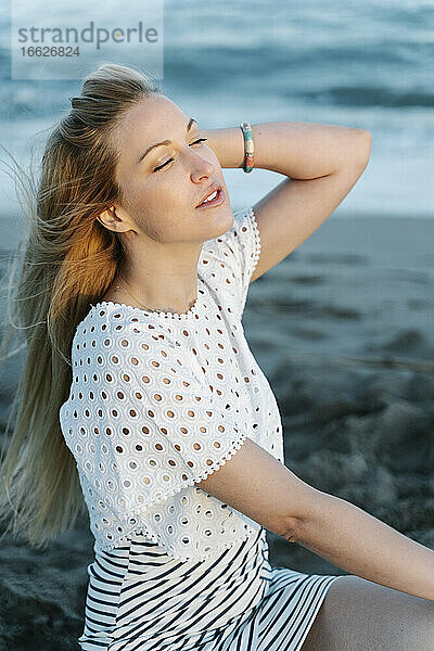Junge Frau mit Hand im Haar am Strand sitzend