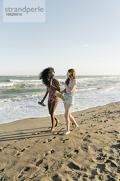 Junge Freunde genießen beim Spaziergang am Strand während eines sonnigen Tages