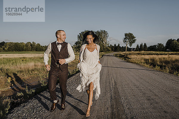 Glückliche Braut und Bräutigam laufen auf der Straße an einem sonnigen Tag