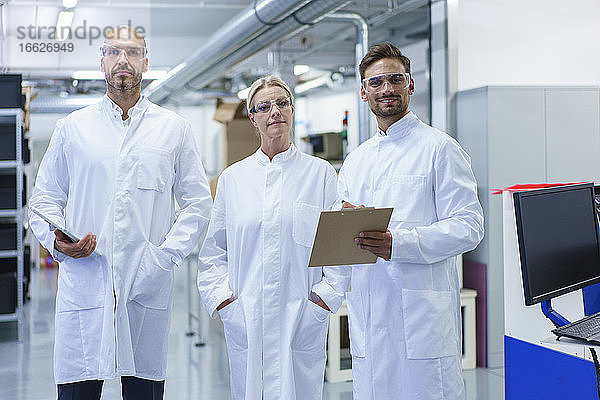 Selbstbewusste männliche und weibliche Wissenschaftler in weißen Laborkitteln stehen in einem beleuchteten Labor