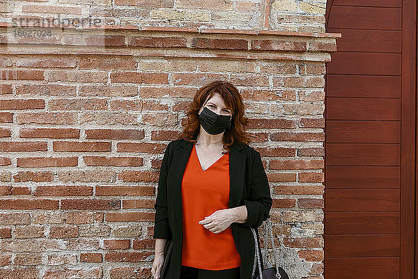 Frau mit Gesichtsschutzmaske  die in einer Stadt an einer Mauer steht