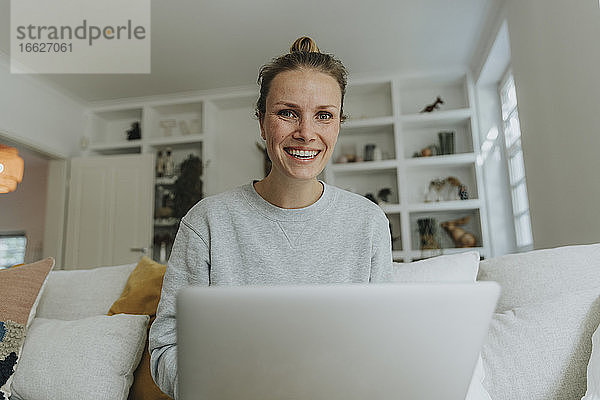 Frau lächelnd bei der Arbeit am Laptop zu Hause