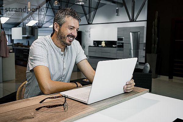 Lächelnde männliche Fachkraft  die auf einen Laptop schaut  während sie freiberufliche Arbeit im Büro erledigt