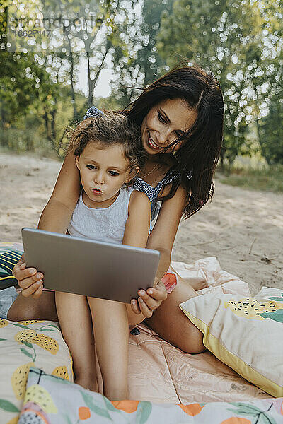 Mutter und Tochter benutzen digitales Tablet am Strand