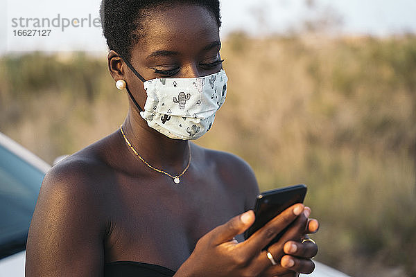 Junge Frau mit Gesichtsmaske  die ein Mobiltelefon benutzt  während sie in einem Archiv steht