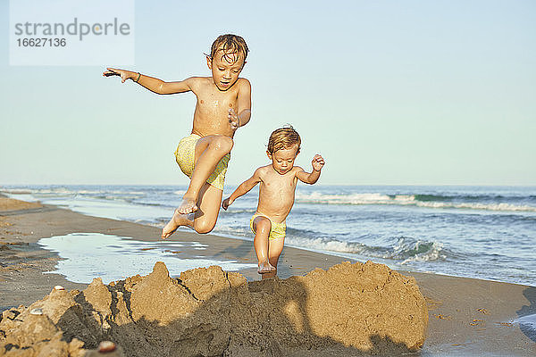 Jungen springen beim Spielen am Strand in den Sand