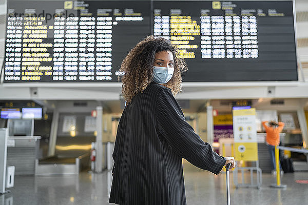 Frau mit Gesichtsschutzmaske schaut über die Schulter  während sie am Flughafen steht