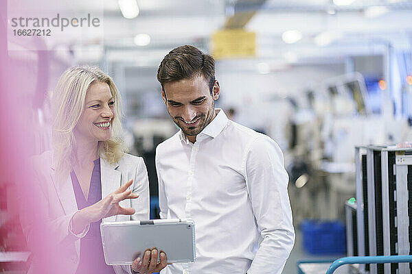Lächelnde Geschäftsfrau im Gespräch mit einem jungen männlichen Kollegen in einer beleuchteten Fabrik
