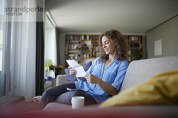 Frau liest Zeitung  während sie zu Hause auf dem Sofa sitzt