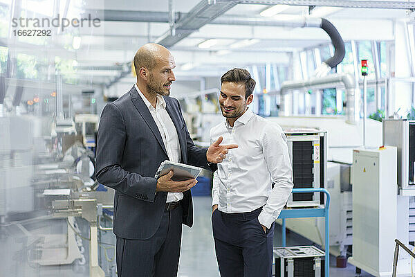 Selbstbewusster Geschäftsmann diskutiert mit einem Ingenieur über ein digitales Tablet in einer Fabrik