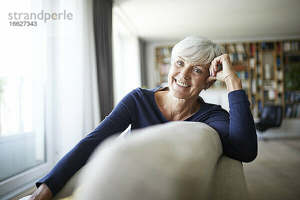 Lächelnde ältere Frau  die auf dem Sofa sitzt und sich entspannt