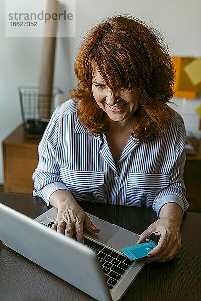 Lächelnde Frau beim Online-Shopping am Laptop  während sie zu Hause sitzt
