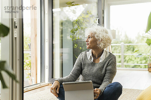 Reife Frau  die ein digitales Tablet benutzt  während sie zu Hause sitzt