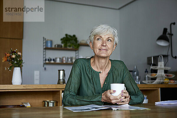Nachdenkliche ältere Frau sitzt mit einer Kaffeetasse zu Hause