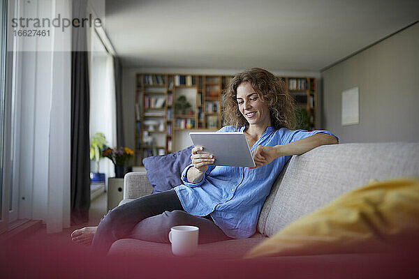 Frau benutzt digitales Tablet  während sie zu Hause auf dem Sofa sitzt