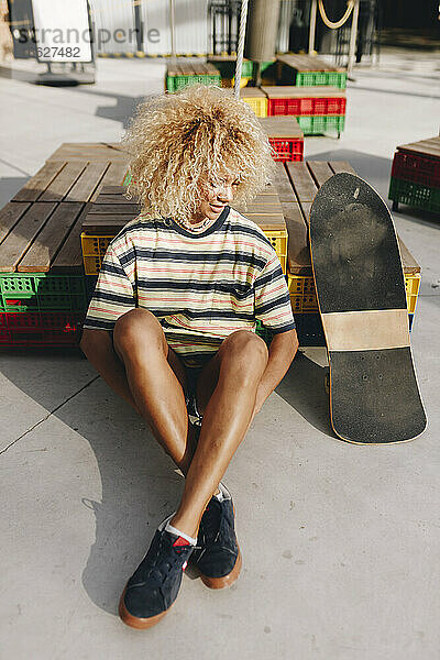 Afro blonde Frau sitzt am Skateboard an einem sonnigen Tag