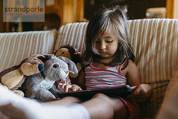 Mädchen benutzt digitales Tablet  während sie zu Hause auf dem Sofa sitzt