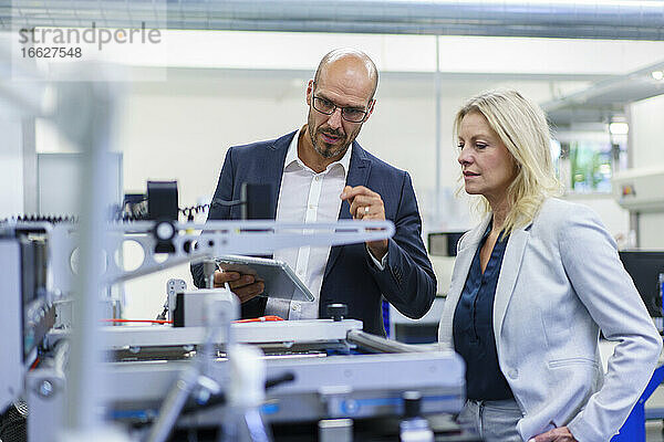 Ein selbstbewusster Geschäftsmann und eine Geschäftsfrau diskutieren  während sie sich Maschinen in einer Fabrik ansehen