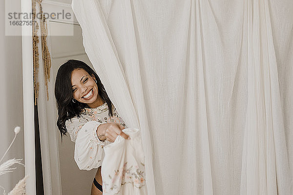 Lächelnde Braut beim Umkleiden hinter einem Vorhang