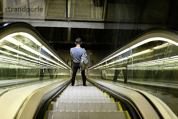 Junger Mann mit Rucksack steht auf beleuchteter Rolltreppe in der U-Bahn
