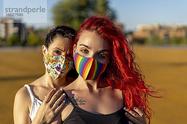 Freunde tragen eine mehrfarbige Gesichtsmaske  während sie an einem sonnigen Tag im Freien stehen