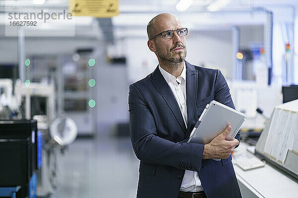 Geschäftsmann  der ein digitales Tablet hält  während er in eine helle Fabrik blickt